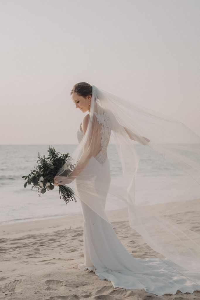 Bride on a Thailand beach holding a bouquet with her veil in the wind