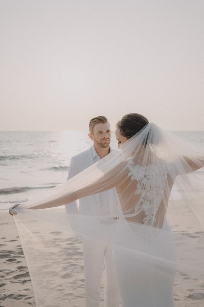 Couple on the beach at sunset with the bride’s veil blowing around them