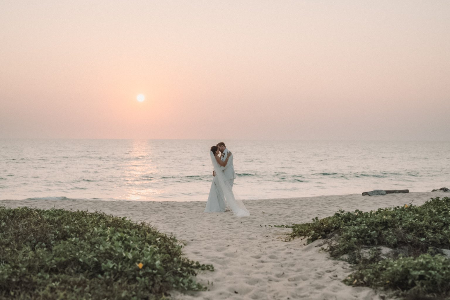 bride and groom kiss during the sunset on the beach in Phuket, Thailand.