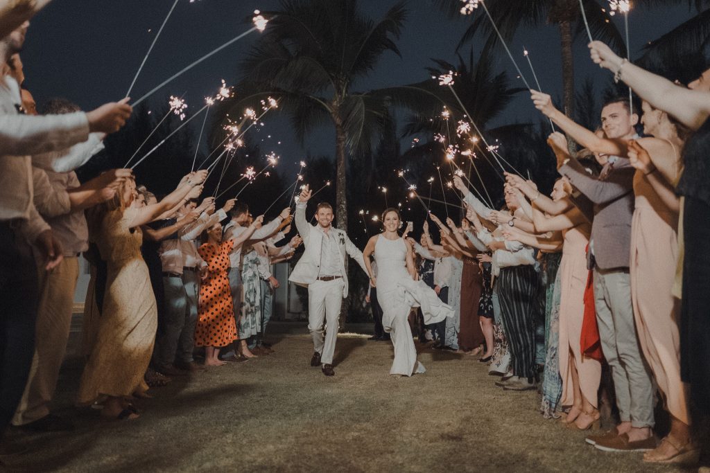 Newlyweds running through a tunnel of sparklers at a night exit