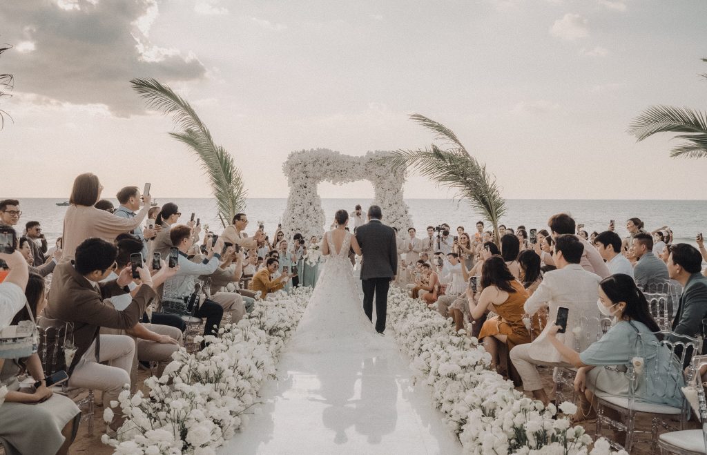 Wedding ceremony on a Thailand beach with guests seated along a floral aisle
