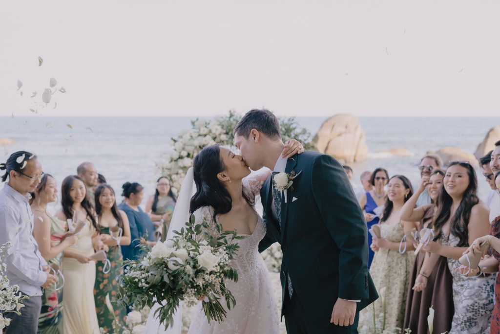 Bride and groom kissing as they walk down the aisle at their destination wedding in Koh Samui, Thailand at the Salavadee Resort.