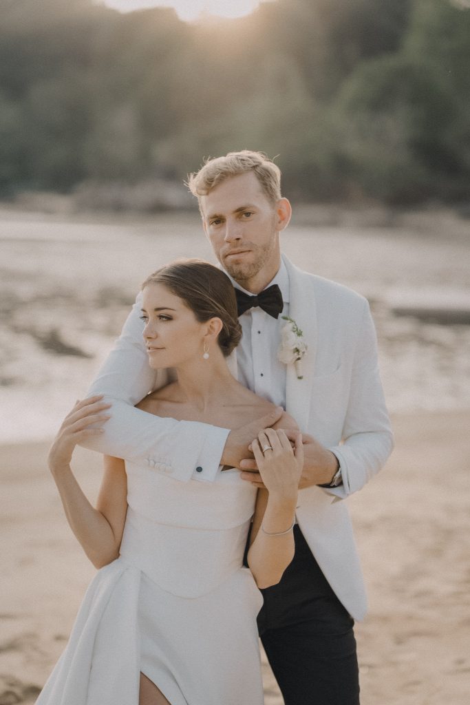 Groom in a white dinner jacket embracing his bride on a Thailand beach