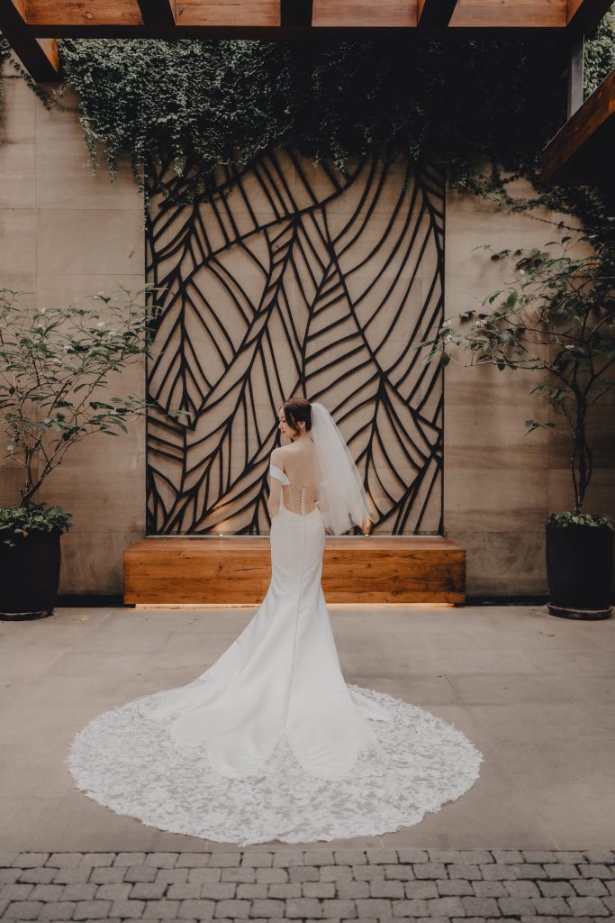 Bride in a lace gown with a long train standing in a stone and leaf-patterned villa courtyard